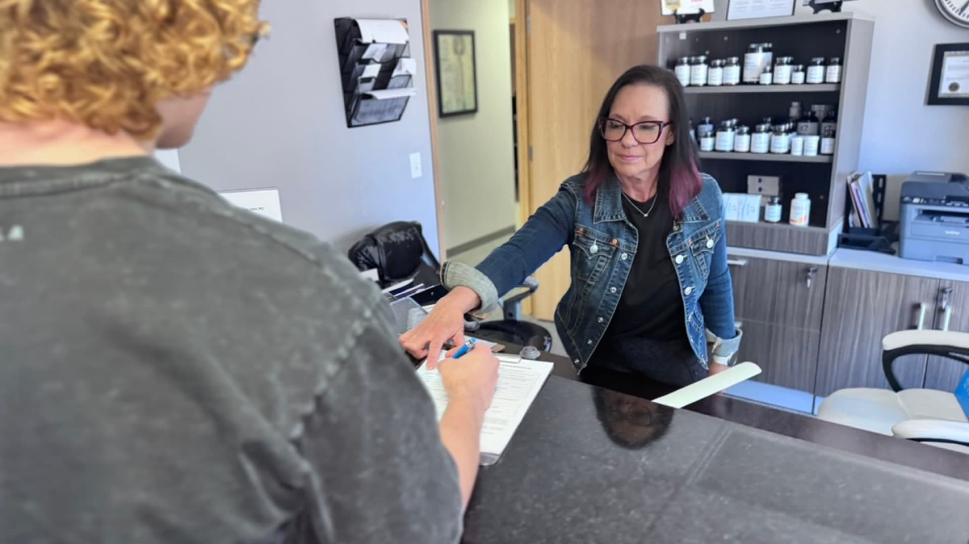 Jamie handing a clipboard to a patient at the front desk of Advanced Chiropractic and Neurology in Omaha, NE
