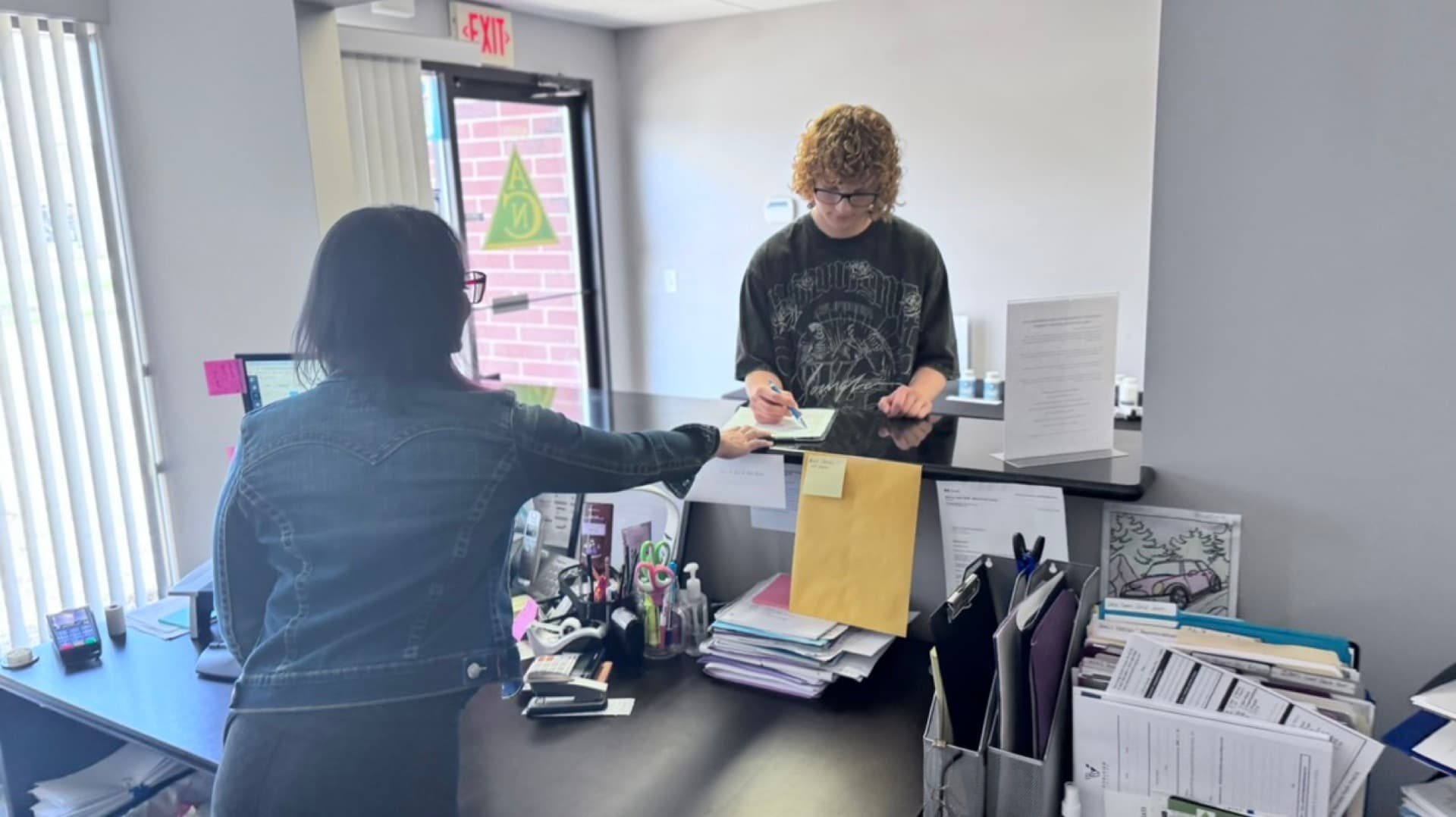 Jamie handing patient forms at the reception window at Advanced Chiropractic and Neurology in La Vista, NE